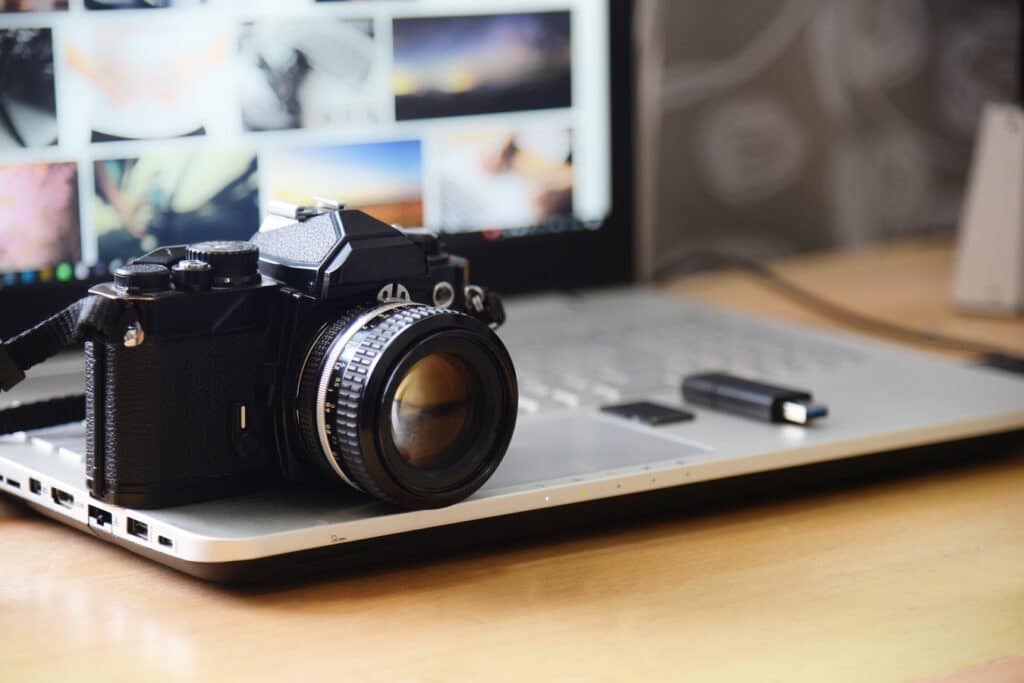 black camera resting on an open laptop beside an sd card and thumb drive