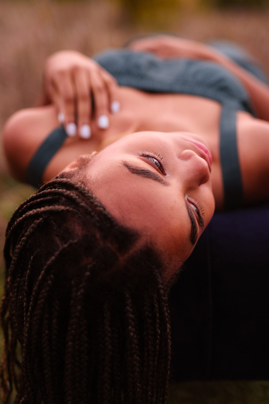 Young woman with long braids, lying down, looking upward; wearing a teal sleeveless top