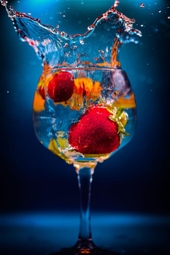 Strawberries submerged in water splashing in a stemmed glass against a dark blue background