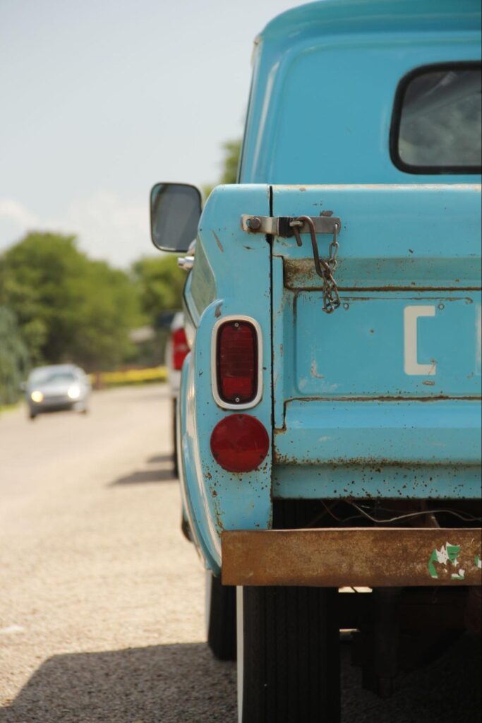Rear view of a rusty, light-blue vintage pickup truck