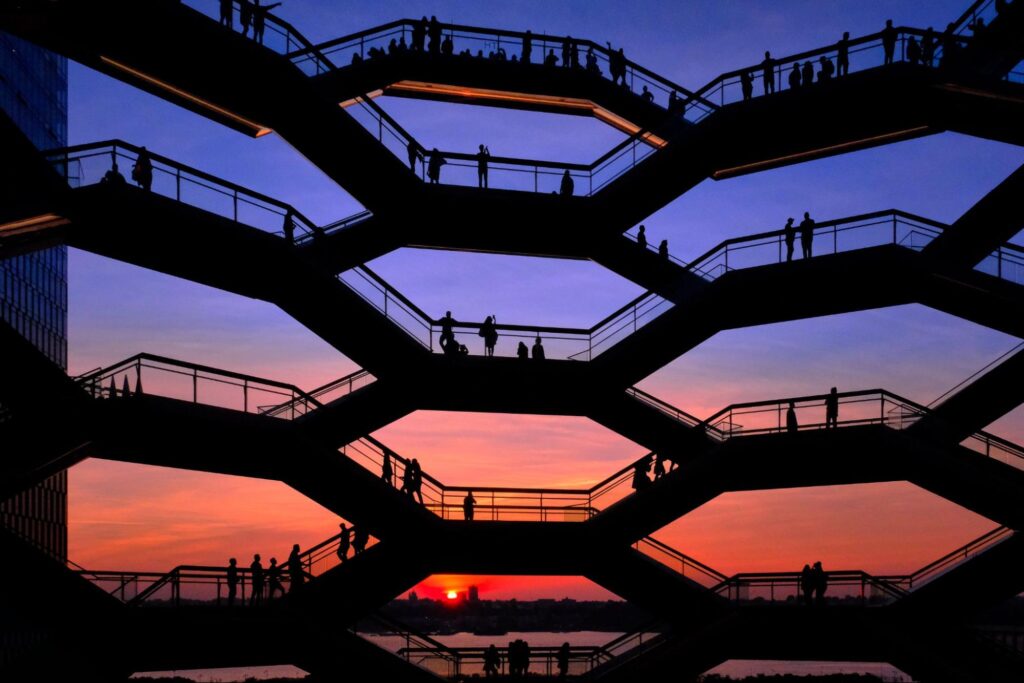 Silhouetted figures on a honeycomb-shaped staircase at sunset, overlooking a cityscape
