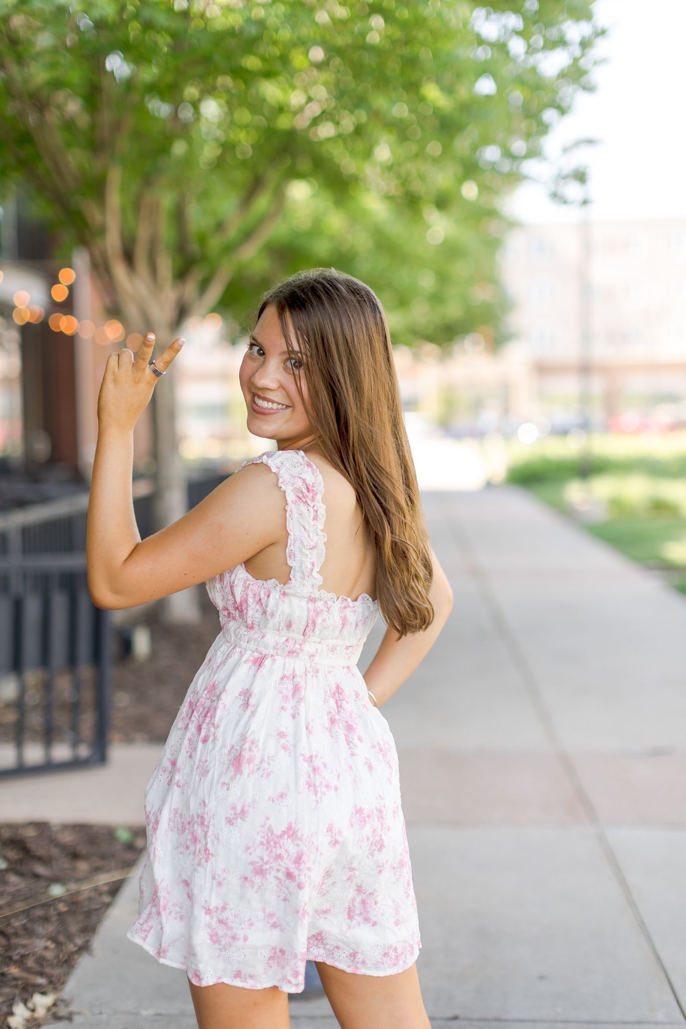 Woman smiling and posing in a pink floral dress on an outdoor walkway