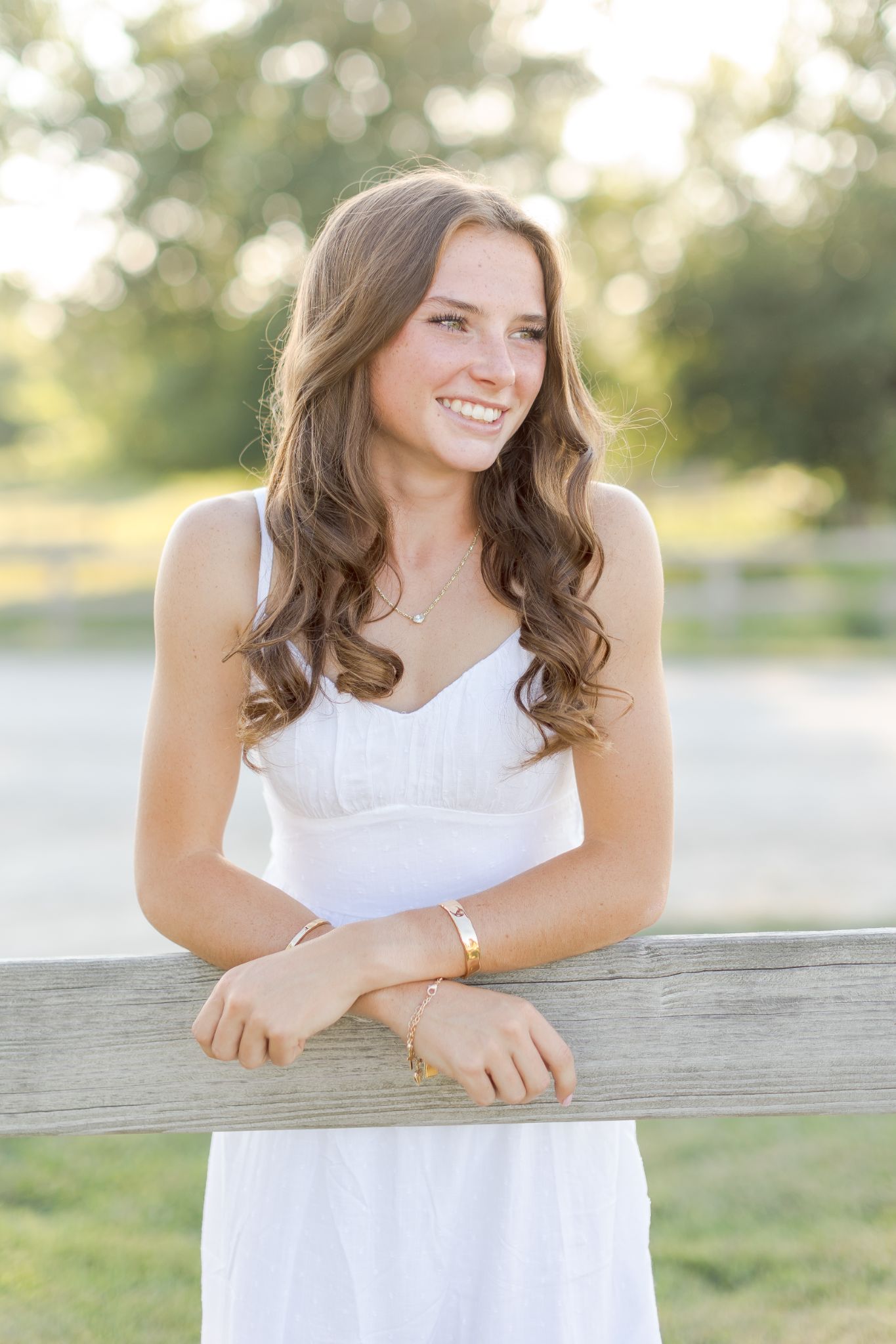 Smiling woman in white dress leaning on a wooden fence outdoors