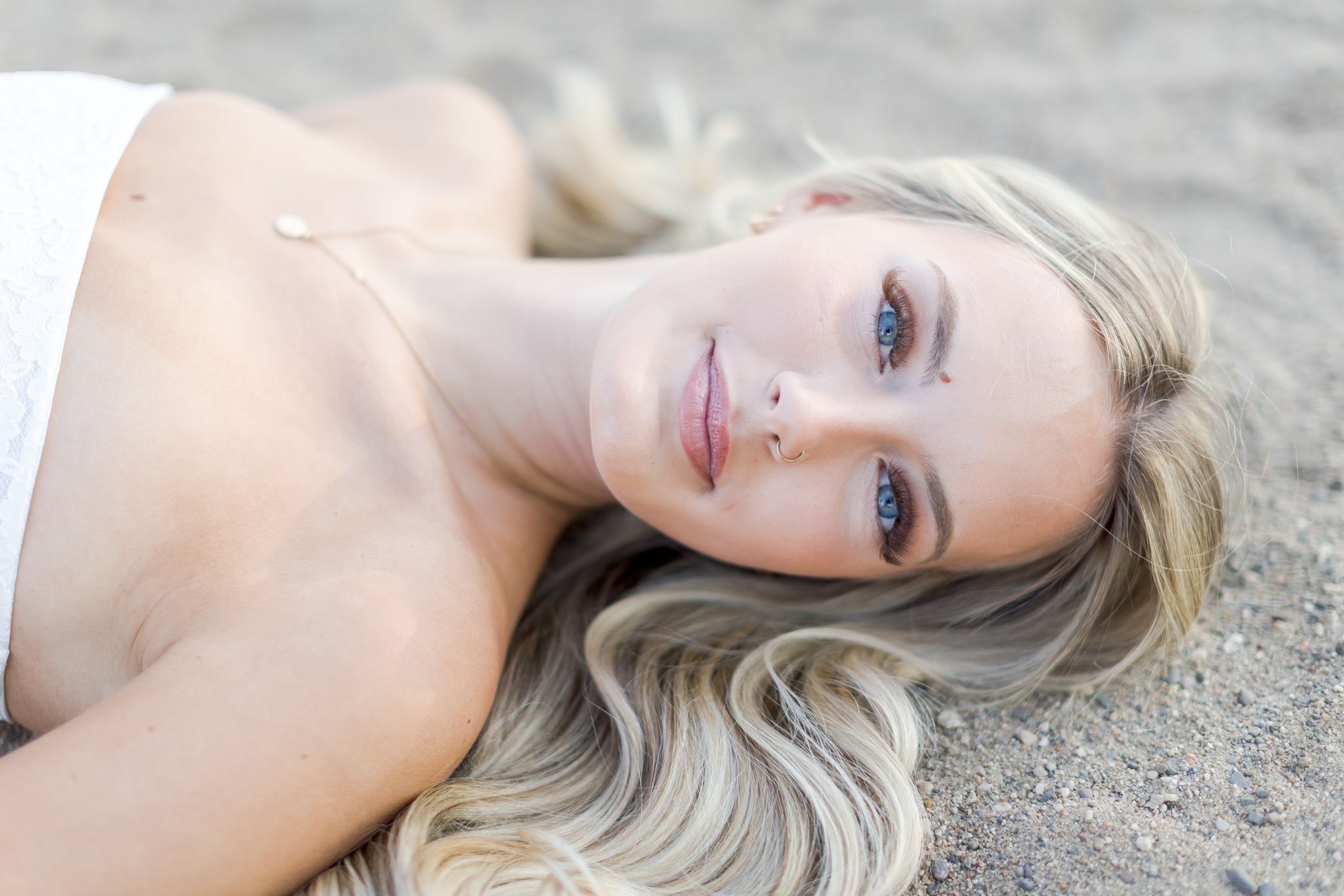 Close-up portrait of a blonde woman with blue eyes lying on a pebbled beach